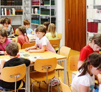 ein Raum mit Bücherregalen und Kindern an Tischen